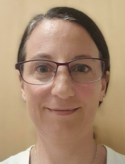 Eine Frau mit Brille und weißem Hemd lächelt in die Kamera.