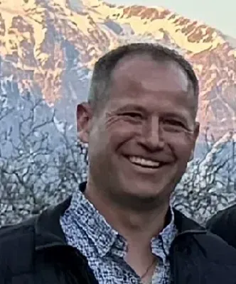 Ein Mann in einer schwarzen Jacke lächelt in die Kamera