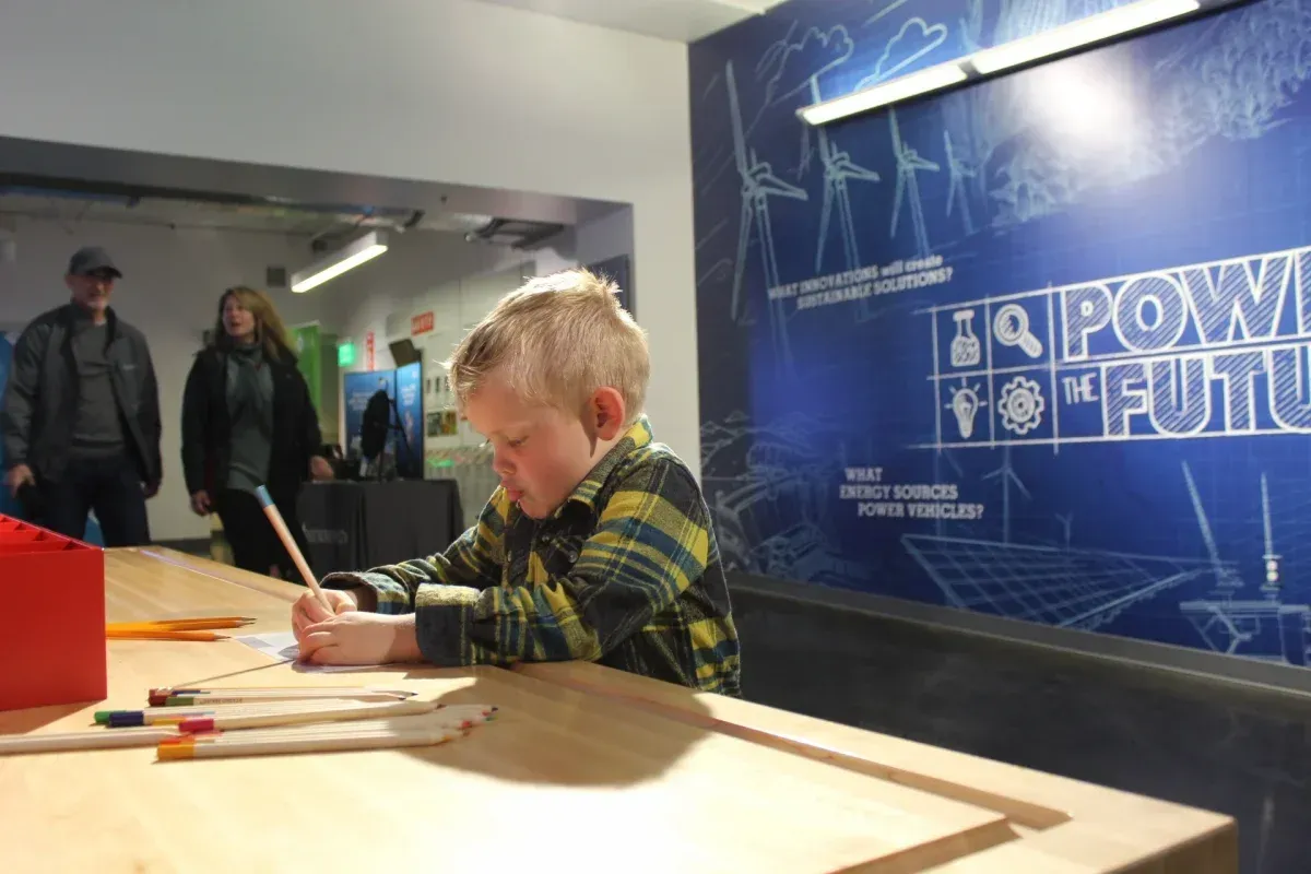 A young boy is sitting at a table drawing on a piece of paper.