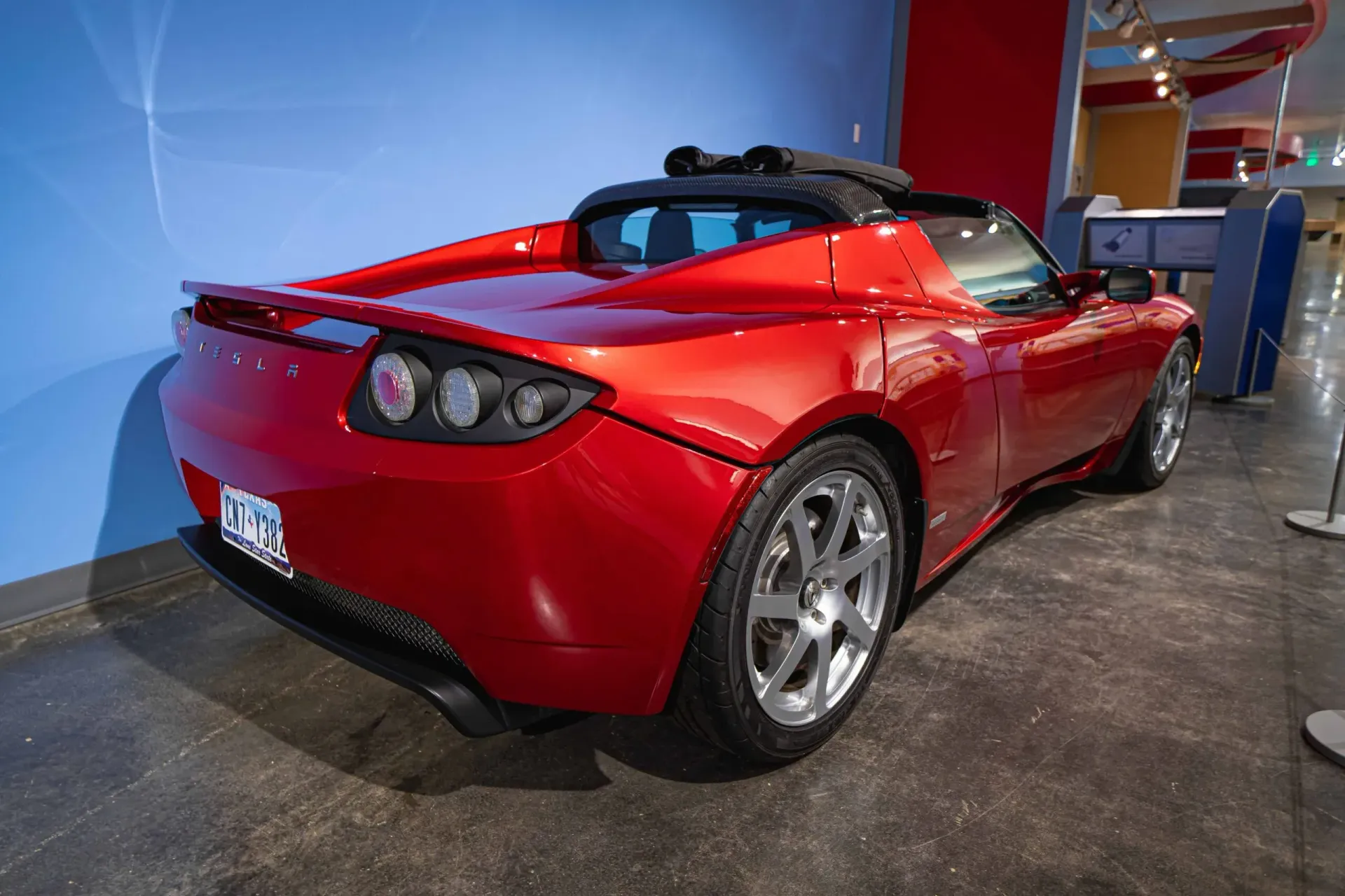 A red tesla roadster is parked in a museum.