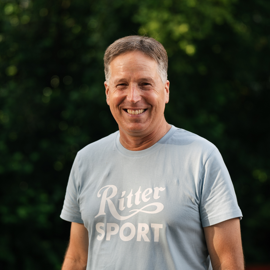A man wearing a ritter sport shirt smiles for the camera