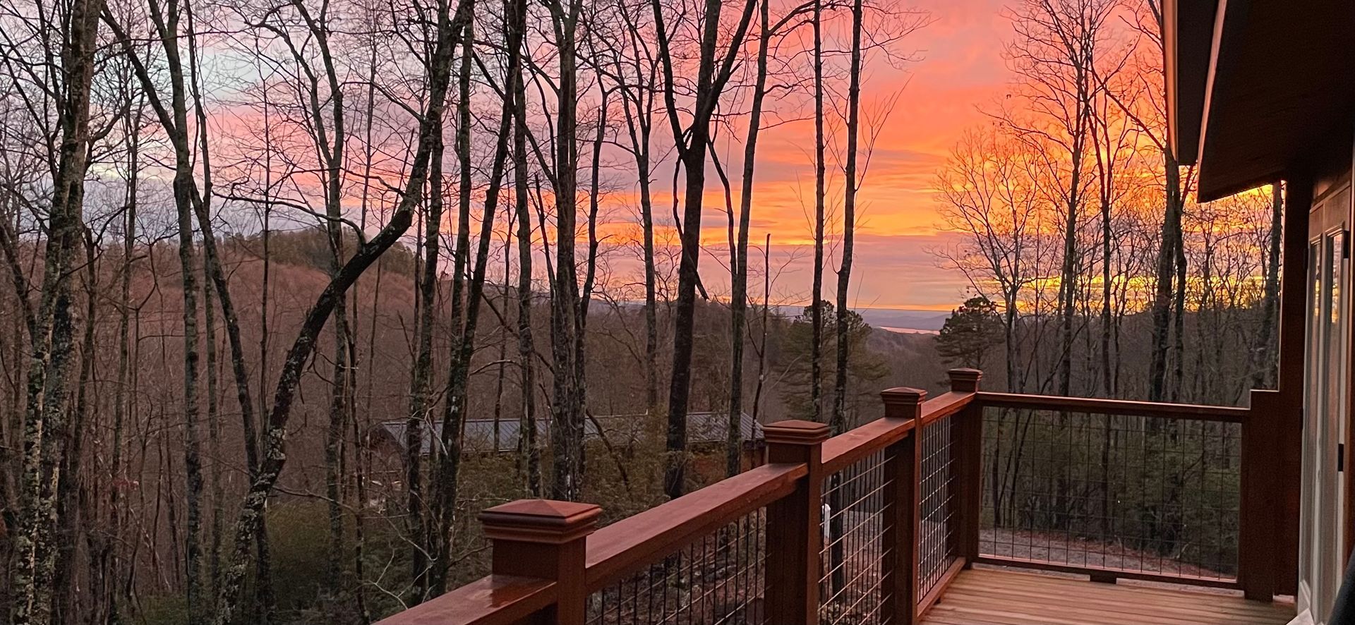 A deck with a view of a sunset over a forest.