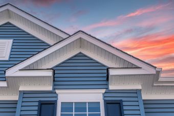 The front of a blue house with a sunset in the background.
