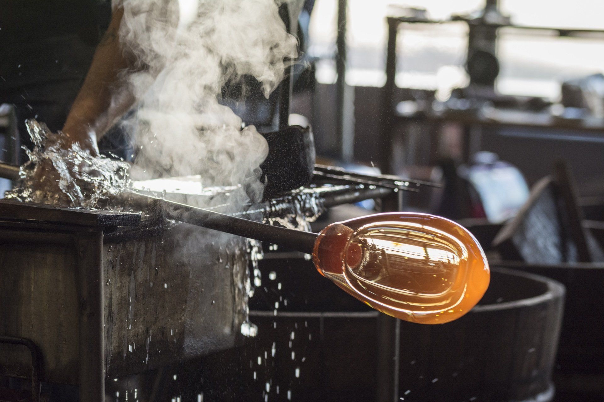 A person is blowing glass in a factory with smoke coming out of it.
